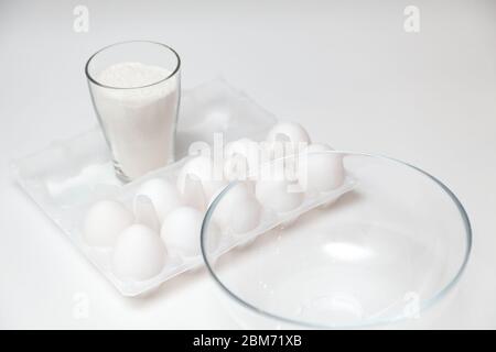A deep empty plate next to a pack of a dozen eggs and flour before cooking on a white isolated background. Food and cooking. Stock Photo