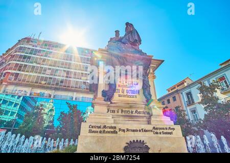 GRANADA, SPAIN - SEPTEMBER 25, 2019: The sun rays on the bronze statue of Catholic Monarchs (Reyes Catolicos) with fountains on both sides of the monu Stock Photo