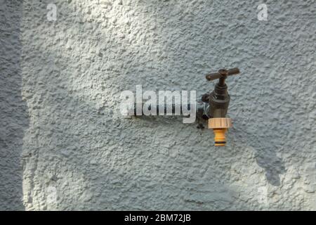 Front view outdoor water tap fitted against outside white painted textured wall. Stock Photo