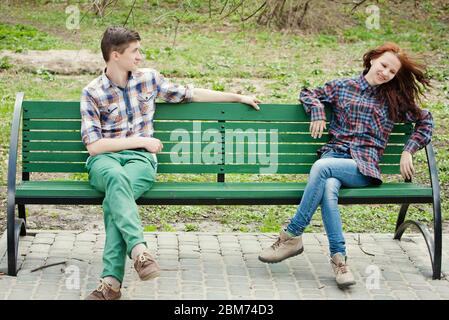 Flirting young couple in plaid shirts sitting on a bench in the park Stock Photo