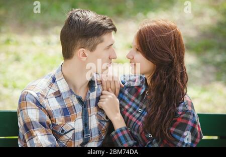 Flirting young couple sitting on a bench in the park and looking into each other's eyes Stock Photo