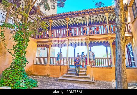 GRANADA, SPAIN - SEPTEMBER 25, 2019: The wooden terrace faces the Patio of the Wrought Iron Grille (Nasrid Palace, Alhambra) with shady trees, on Sept Stock Photo