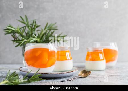 homemade panna cotta with slices of peach and peach jelly in glass jars on a gray concrete background. Stock Photo