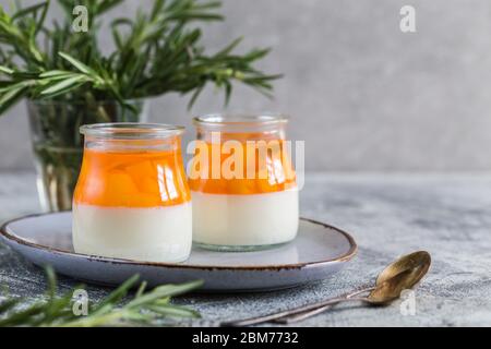 homemade panna cotta with slices of peach and peach jelly in glass jars on a gray concrete background. Stock Photo