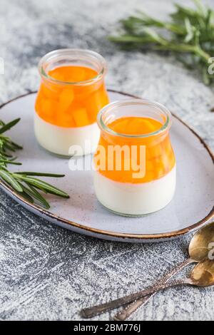 homemade panna cotta with slices of peach and peach jelly in glass jars on a gray concrete background. Stock Photo