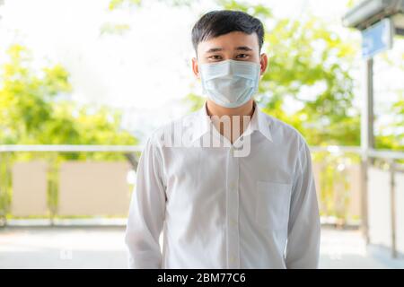 Young Asian businessman in white shirt going to work in pollution city she wears protection mask prevent PM2.5 dust, smog, air pollution and COVID-19 Stock Photo