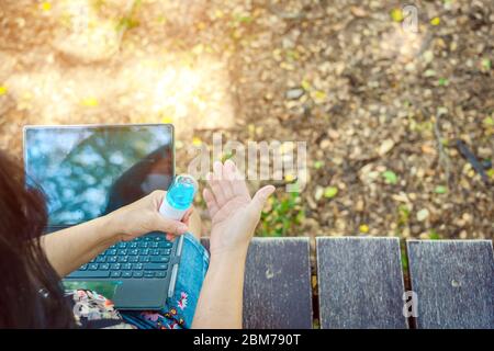 Woman using alcohol nano mist sprayer cleaning her hand before work with laptop to prevent the virus and bacterias. Quarantine for coronavirus (Covid- Stock Photo
