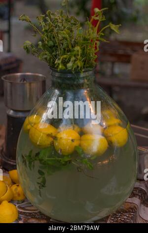 Homemade lemonade in a large glass vase, seasoned with mint leaves and whole lemons and lemon peel.