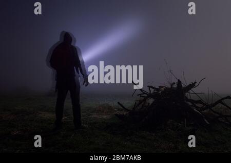 A spooky double exposure of a hooded figure, shining a torch in a foggy winters night. Stock Photo