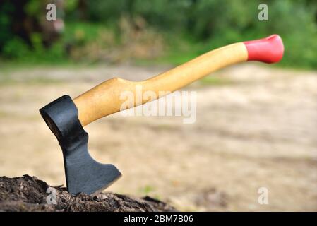 a beautiful-shaped ax sticks out in a tree, with a yellow handle close-up, on a natural background Stock Photo