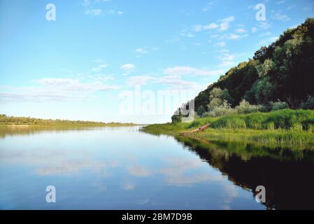 old wooden boat on the river bank close up against the background of green grass and bushes, reflections in the water Stock Photo