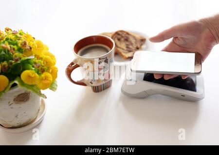 Contactless payment through mobile cell phone at cafe. Customer paying on pos terminal at counter in coffee shop. Stock Photo