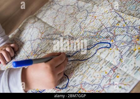 Hand of the child writing on a map with blue pen. Kids hand holding felt-tip pen. Travel and vacation  with children. Summer rest concept. Stock Photo