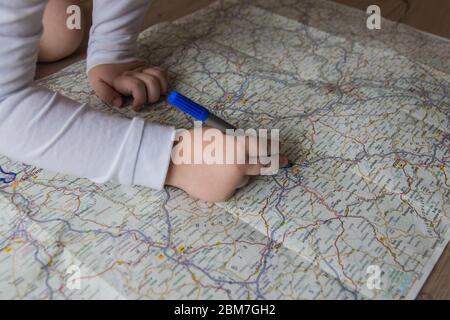 Hand of the child writing on a map with blue pen. Kids hand holding felt-tip pen. Travel and vacation  with children. Summer rest concept. Stock Photo