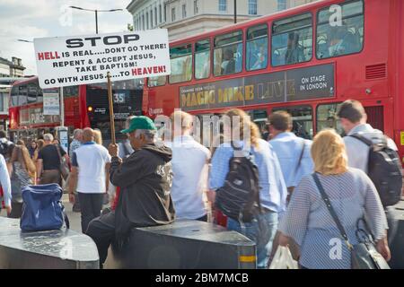 An evangelical Christian holds a sign urging people to repent and go with Jesus as commuters stream past on their way home across London Bridge, UK Stock Photo