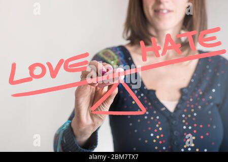 Conceptual image of a woman drawing a seesaw showing an imbalance between word Love being weighted more than the word Hate on opposites ends. Stock Photo