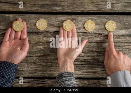 Hands of three business people with Bitcoins laid out in a row on a rustic wood background conceptual of investing in the cryptocurrency. Stock Photo