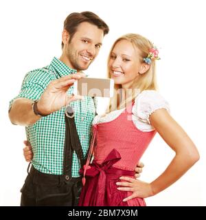 Happy couple in traditional Bavarian clothes photograph themselves with a smartphone Stock Photo