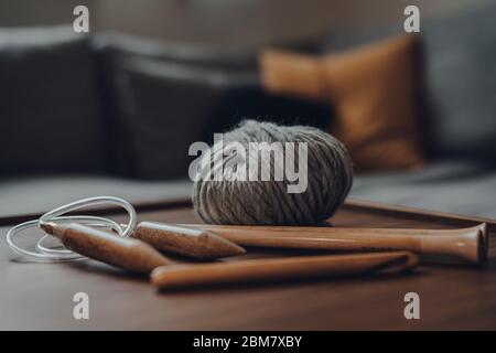 Close up of a ball of grey chunky wool yarn and a variety of maker tools on a wooden table, shallow focus. Stock Photo