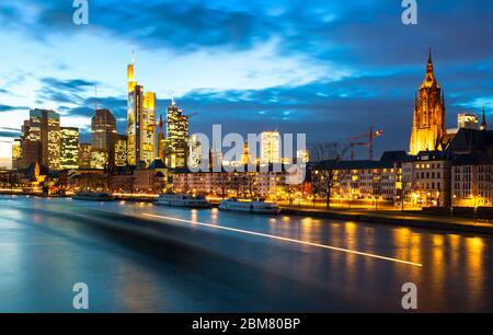 Dusk on the Main as a barge passes in Frankfurt am Main, Hesse, Germany. Frankfurt is a metropolis and the largest city of the German federal state of Hesse, and its 746,878 (2017) inhabitants make it the fifth-largest city in Germany. Stock Photo