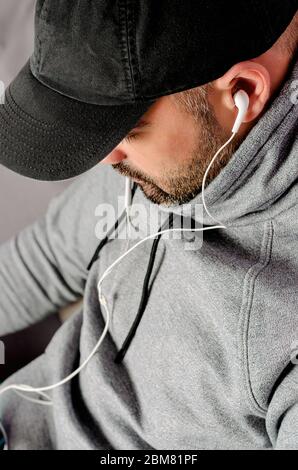 Cropped portrait of bearded man in black cap watching videos or listening to the music with earphones. Stock Photo