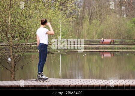 Roller skating, slim girl in jeans standing on rollers in a spring park. Concept of sports, vitality, healthy lifestyle Stock Photo