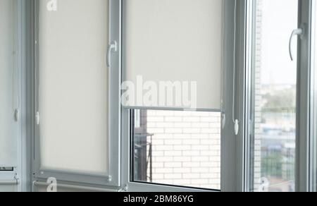 Details of white fabric roller blinds on the plastic window with wood texture in the living room Stock Photo