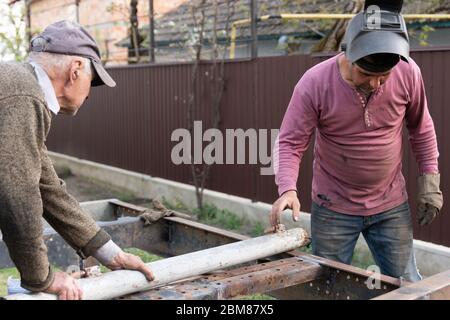 Two welders at work into the construction site, man with his father working with metal in the backyard Stock Photo