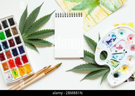 Set of watercolor paints, art brushes, palette and blank album. Marijuana leaf. Cannabis reveals creativity. The concept of art. Stock Photo