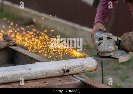 A young man welder processes a metal product with a angle grinder in the garage Stock Photo