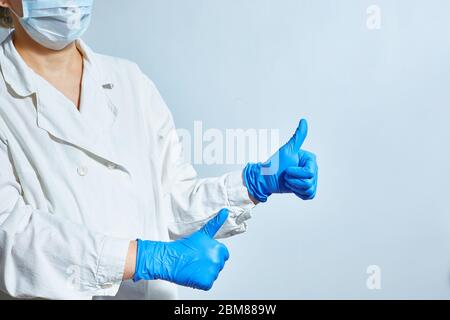 A nurse in protective gloves and a white doctors lab coat in a face mask shows that everything is fine. Copy space. Stock Photo
