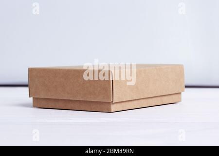 Cardboard box. Package isolated on white wood background. Craft paper box side view. Small square closed cardboard. Shipping eco package. Delivery Stock Photo