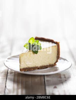 Slice of classic New York cheesecake with a sprig of mint on a plate on a wooden table. The concept of bakery and sweet cakes desserts Stock Photo