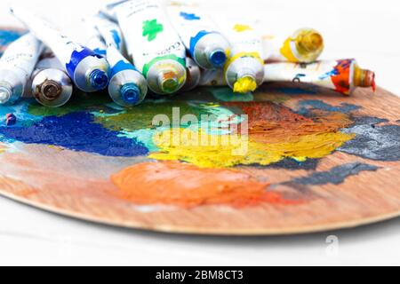 Artists oil paint tubes open and used on a wooden palette,  with mixed colours.  Art and craft supplies concept Stock Photo