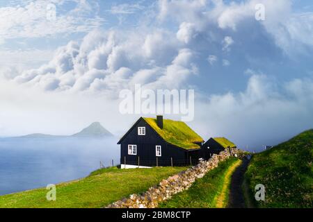Foggy morning view of a house with typical turf-top grass roof and blue cloudy sky in the Velbastadur village on Streymoy island, Faroe islands, Denmark. Landscape photography