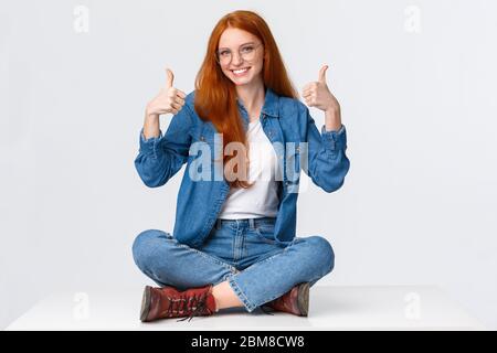 Excellent, satisfaction and people concept. Delighted supportive cute redhead girlfriend sitting on floor, with legs crossed in relaxed pose, smiling Stock Photo