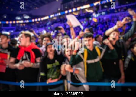 Blurred background of an esports event - A lot of fans on a tribune at tournament's arena with hands raised. Cheering for their favorite team. Stock Photo