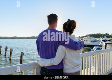 Rear view of young multi ethnic couple hugging together at the pier outdoors Stock Photo