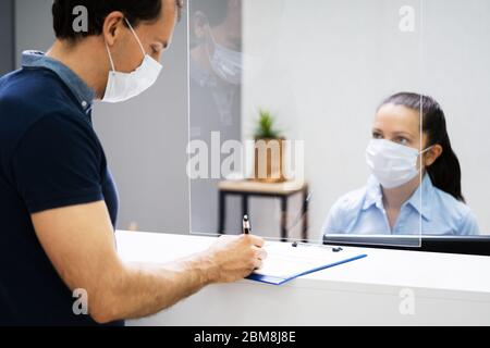 Client Signing Paper At Reception Desk In Face Mask Stock Photo