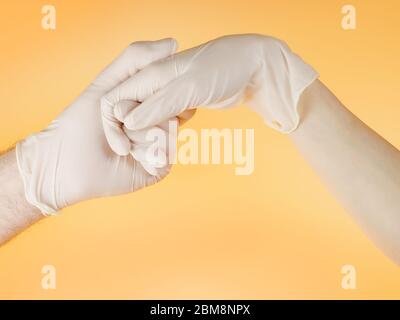 Man and woman hands in white protective gloves holding one another. On light yellow background Stock Photo
