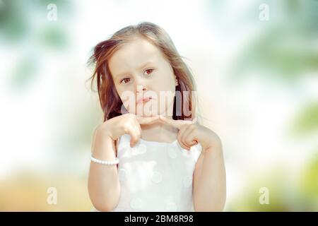 Portrait of a cute kid girl looking at camera unhappy and upset outdoors green tree park on background Stock Photo