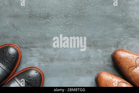 Top view of black and brown leather men boots with water drops on wet grunge navy blue background, copy space, flat lay. Warm shoes for autumn weather Stock Photo