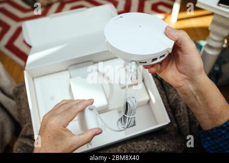 Paris, France - Circa 2020: Senior holding unpacking new parcel from Amazon Prime containing latest TP-Link Deco M9 Plus AC2200 Smart Home Mesh Wi-Fi System to be used for teleworking Stock Photo