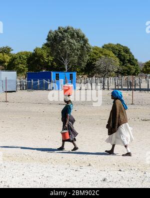 Two African woman walking with water buckets on their heads, walking to a village in Namibia, Africa. Stock Photo