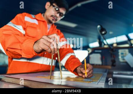 Filipino deck Officer on bridge of vessel or ship. He is plotting position on chart Stock Photo