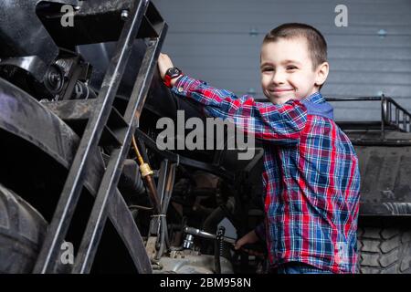 Little boy young auto mechanist cheerfully dreams that he   rides fast on a motorcycle in the garage of a service station. A child smiling and standin Stock Photo
