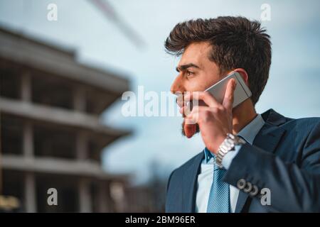 Young male construction engineer or businessman talking on phone looks at his wrist watch Civil engineer,construction Plan Stock Photo