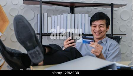 Senior Asian man using smart phone shopping online and paying with credit card at home Stock Photo