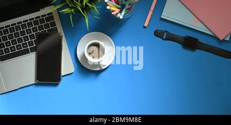 Top view image of computer laptop putting on colorful working desk with coffee cup, potted plant, pencils in glass vase, smartphone, note, smartwatch Stock Photo