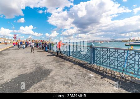 Tourists pass by local Turkish fisherman fishing in the Bosphorus River along the Galata Bosphorus bridge at the Golden Horn in Istanbul, Turkey Stock Photo